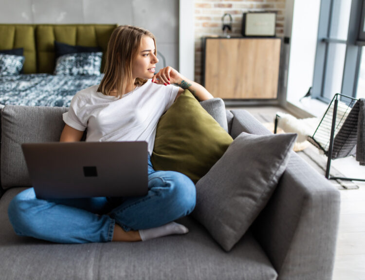 A girl is sitting on a sofa with a laptop